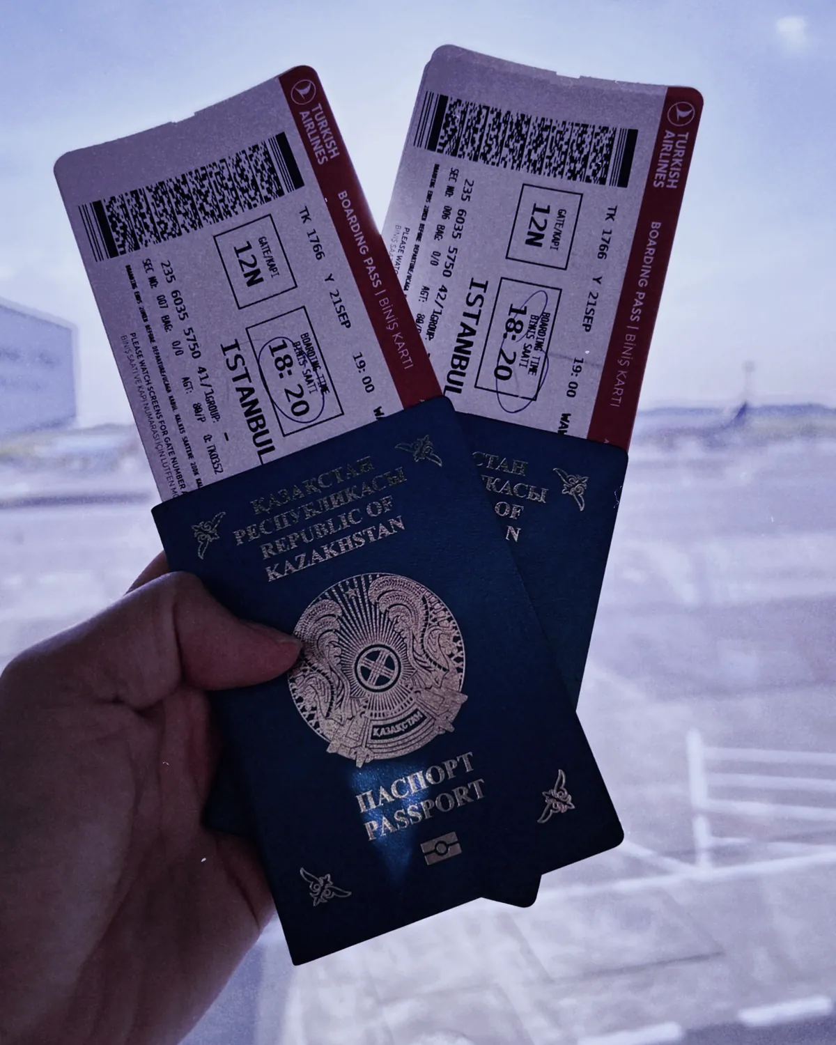 Putnik drži pasoše i boarding karte ispred aerodromskog prozora